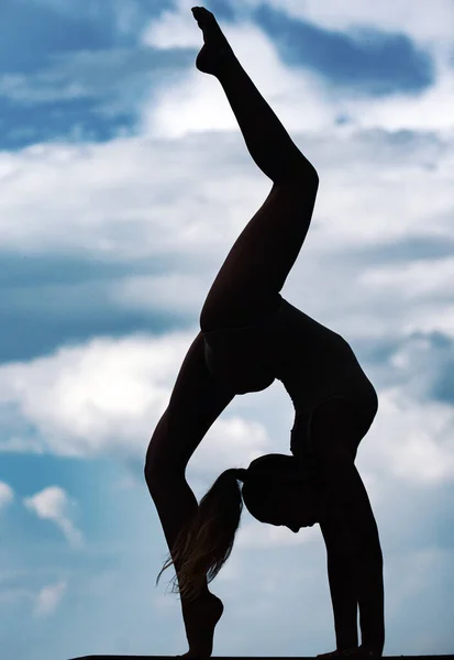 女子体操在天空中的轮廓 一个身材苗条的小女孩在做杂技表演 背光下的体操 — 图库照片