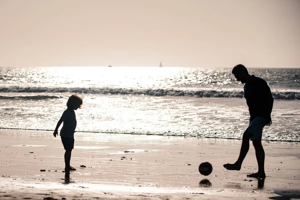 父と息子は夏休みにビーチでサッカーやサッカーをします 日没の屋外シルエットを楽しむお父さんと子供 — ストック写真