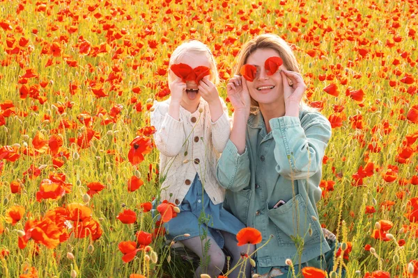 Happy spring family. Mother and daughter walking through a flowering poppy field. Summer family holidays on nature. Summer on poppies meadow with poppys flowers. Closing eyes with flovers. Hides eyes