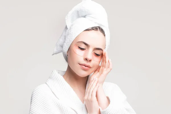 Woman applying eye patches. Calm relaxed woman has fresh healthy skin, keeps eyes shut, wears collagen patches under eyes, wears towel on head, gets facial treatment