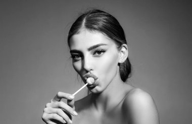 Kırmızı dudaklı bir kadın lolipop yalıyor. Temiz ciltli güzel bir genç kadın. Şehvetli bir kadın. Modaya uygun. Muhteşem dişiler şekerleri emerler. Güzel moda portresi.