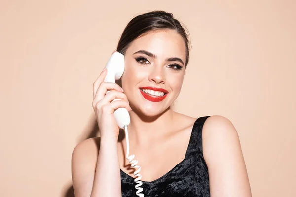 年轻的微笑的女人通过复古电话交谈 有老式电话接收机的女人在演播室用米色背景隔离的带复古电话耳机的女孩 — 图库照片