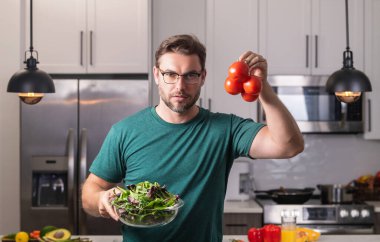 Genç adam mutfakta vegan sağlıklı salata pişiriyor. Modern mutfak masasında milenyum adamı sebze doğruyor, akşam yemeği ya da öğle yemeği için taze sebze salatası hazırlıyor. Sağlıklı beslenme, vejetaryen konsepti