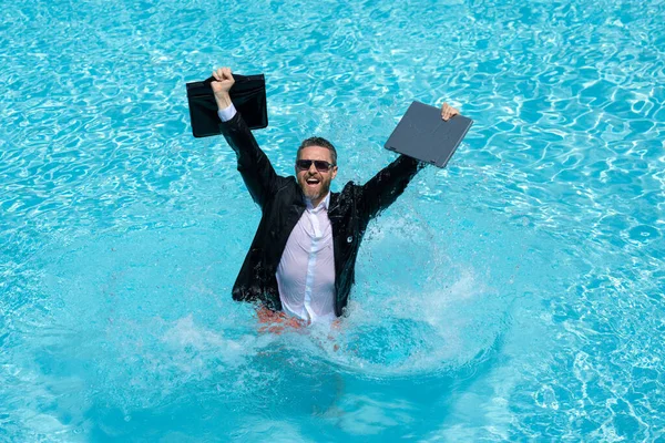 stock image Business man in suit with laptop excited jumping in swimming pool. Summer travel tourism and business concept. Crazy office employee using laptop in pool on summer day