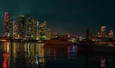 Alacakaranlıkta şehir gökdelenleri ve deniz üzerinde köprü olan Miami City Skyline Panorama 'sı. Miami şehir merkezi gece manzarası