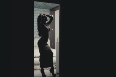 Uzun ince elbiseler ve yüksek topuklularla rahatlayan muhteşem bir kadın silueti. Kadın yatak odası girişinin önünde duruyor. Uzun bir gündü. Seksi kadın kahin hazzı rahatla. Rahatlayın. Benimle yatağa gel..