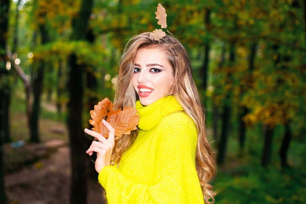 Fashion autumn portrait woman with yellow maple leaves on Nature Background. Pretty woman walking in the Park and enjoying the beautiful autumn nature. Autumn woman having fun at the park and smiling