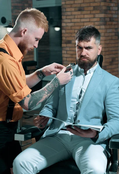 Barber making haircut of attractive bearded man in barber shop. So trendy and stylish. Brutal guy in modern Barber Shop. Hairdresser makes hairstyle a man with a beard. Portrait of stylish man beard