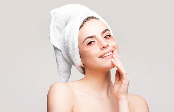 Happy woman applying eye patches. Close up portrait girl with towel on head. Portrait of beauty woman with eye patches showing an effect of perfect skin