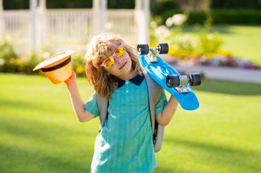 Çocuk pembe arka planda uzun tahta tutuyor. Pennyboard 'u olan çocuk. Bozuk paralı neşeli küçük bir çocuğun açık hava portresi. Yaz çocukları modası
