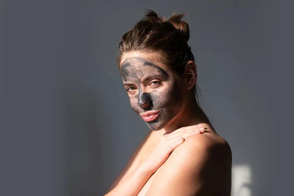 裸の肩と粘土マスクをした若い女性が顔に 顔に化粧品クリーム処理を適用する美しいモデル 顔の治療 黒粘土マスクと裸の肩を持つトップレス女性 — ストック写真