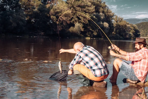友人釣りと熟女先輩 夏休みだ 幸せな陽気な人々 髭を生やした男が魚を捕まえる 釣り竿を持つ漁師 活動と趣味 魚を捕まえる — ストック写真
