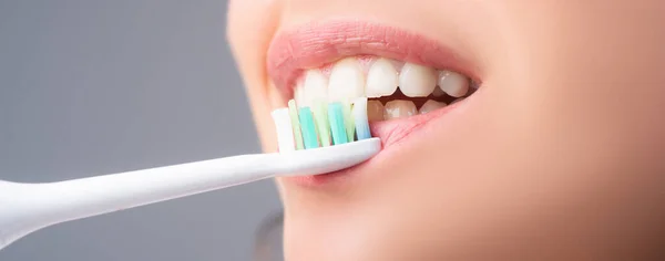Close-up mouth with teeth-brush. Human teeth. Dental health care clinic. Close-up of a young woman is brushing her teeth. Banner, copyspace