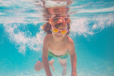 Çocuk yaz havuzunda su altında yüzer. Yaz çocukları tatil konsepti. Komik çocuklar yüzlerini suyun altına çevirir. Yüzme havuzunda su sıçratan çocuk. Yaz sporu. Çocukla yaz tatili