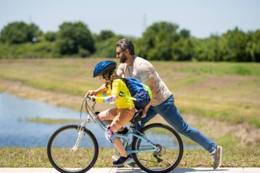 Babalar Günün kutlu olsun. Bisiklet kasklı baba ve oğul parkta bisiklet sürmeyi öğrendikleri için. Baba oğlunun bisiklete binmesine yardım ediyor. Baba ve oğul yaz günü bisiklete biniyor. Oğlu babasıyla bisiklete binmeye çalışıyor.