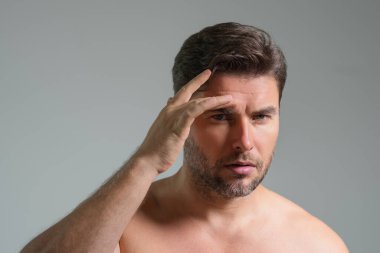 Mükemmel esmer adamın çene ve tenine dokunuşunun yakın plan portresi. Gri stüdyoda yüzüne dokunan yakışıklı bir adam izole edilmiş bir arka plan. Mükemmel cilt. Erkek kozmetik, deri tedavisi. Hijyenik cilt bakımı erkek yüzü