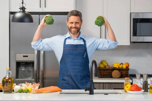 台所でブロッコリーを調理エプロンでハンサムな男 現代のキッチンテーブルチョップ野菜で千年の男は 夕食や昼食のための新鮮な野菜サラダを準備します 健康的な食事 ベジタリアン — ストック写真