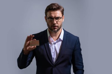 Ciddi kibirli bir iş adamının gri arka planda plastik kredi kartı gösteren portresi. İş ve başarı kavramı. İnternetten alışveriş. Çevrimiçi ödeme. Kredi kartının bakiyesi