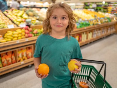 Çocuklar için sağlıklı yiyecekler. Limonlu ve portakallı çocuk. Markette ya da markette elinde poşetle gülümseyen küçük bir çocuğun portresi. Çocuk sebze süpermarketinde meyve seçerken