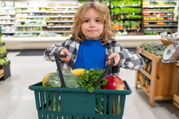 Portrait of child with shopping basket purchasing food in grocery store. Funny kids face. Sales and shopping. Kid buying products at supermarket. Supermarket and grocery shop. Discount, sale concept