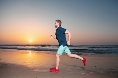 Atletik genç adam koşuyor. Açık hava antrenmanı sırasında deniz batımı geçmişi olan formda bir erkek fitness koşucusu.