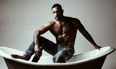 Bu da banyo zamanı demek. Banyoda oturan kas gövde dövmesi ile güçlü latino adam. Atelak İspanyol adam banyoda şarap içiyor. Şarap ve banyo onun için rahatlamanın anahtarıdır..
