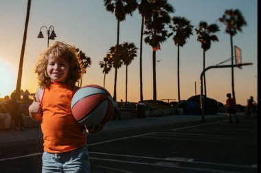 Çocuk gün batımında basketbol topuyla dışarıda oynuyor.