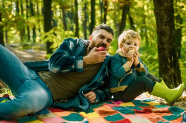 Orman pikniği yürüyüşü. Hipster sakallı baba oğluyla birlikte ormanda vakit geçiriyor. Acımasız sakallı adam ve küçük çocuk elma yiyor. Sağlıklı yaşam tarzı. Doğa pikniği. Sağlıklı atıştırmalık. Vitamin yükü. Aile pikniği.