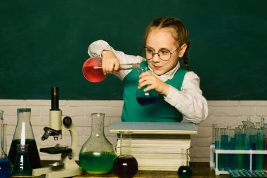 Neşeli gülümseyen küçük çocuk mavi duvarda eğleniyor. İlkokuldan bir çocuk. Çocuk sınıfta tahtayla ilgili bir şeyler öğreniyor. Masada mutlu gülümseyen öğrenci çizimleri