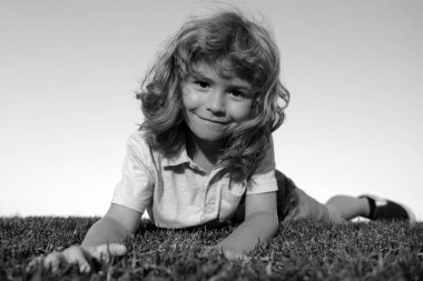 Çocuk yeşil çimlerin üzerinde yatıyor. Mutlu çocuk yeşil bahar tarlasında gökyüzü arka planına karşı oynuyor. Özgürlük çocukları ve hayal gücü kavramı