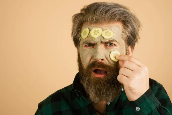 Funny man with facial mask. Man getting facial care with cucumber. Beautician is making facial mask on man face. Cosmetologist making facial skincare procedure