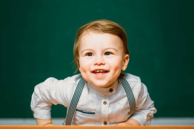 Küçük mutlu öğrenci. Şirin bir anaokulu öğrencisi kapalı bir masada oturuyor. Bireysel ders. Sınıfta, tahtaya yakın arkadaş canlısı bir çocuk.