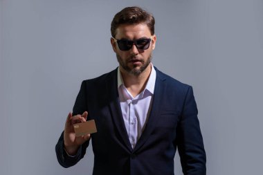 Gri arka planda kredi kartı tutan bir iş adamı. İspanyol adam kredi kartını gösteriyor. Kredi kartı ya da banka kartı. İnternetten alışveriş konsepti. İndirim teklifi, online alışveriş.