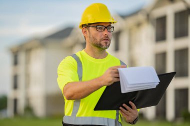 İnşaatçı inşaat alanında. Sert şapkalı bir adam. Yeni bina inşaatında miğferli inşaat işçisi. Pano mühendisi, bina teftişi.