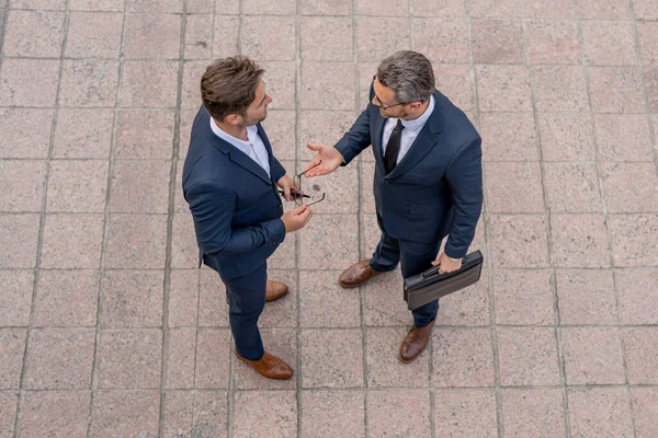 Photo of business partners talk conversation outdoor. Two handsome businessmen in suits discuss a working project against the background of urban city. New projects or startups. Cooperation concept