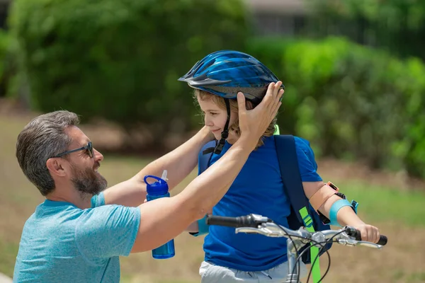 Father teaching son riding bike. Dad helping child son to ride a bicycle in american neighborhood. Father helping his son to wear a cycling helmet. Happy fathers day. Summer sport with child