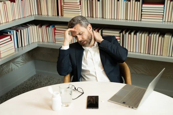 100万人のビジネスマンが頭痛の種だ 自宅のオフィスでラップトップでスーツの仕事をしているビジネスマンは メガネが片頭痛や頭痛に苦しんでいます 頭痛に悩まされて疲れた男 — ストック写真