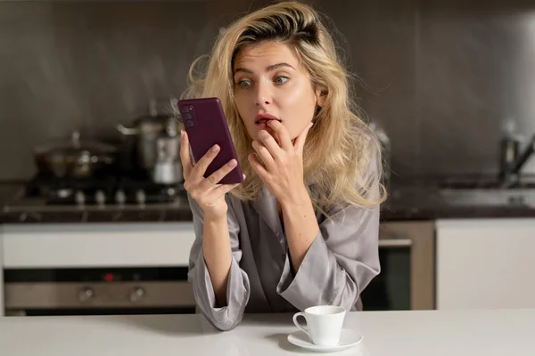 Şaşırmış Bir Kadın Sabah Mutfakta Oturmuş Telefon Izliyor Akıllı Telefonlardan — Stok fotoğraf