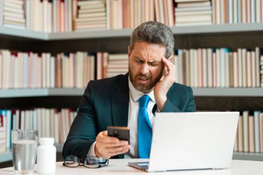 İş adamının ağrısı yüzünden migreni tuttu. Güçlü baş ağrısı olan bir adam dizüstü bilgisayarla çalışıyor. Çok çalışan bir serbest çalışan ya da ofisin müdürü. Stresli, başı ağrıyan yorgun bir adam.