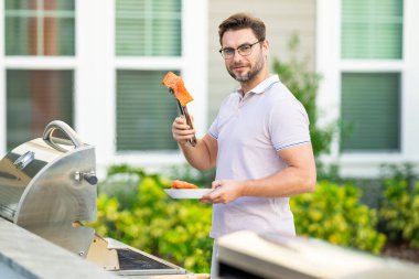 Erkek aşçı bahçede ızgara yapıyor. Barbekü açık hava bahçe partisi. Yakışıklı adam barbekü somonu hazırlıyor. Yaz boyunca dışarıda yemek ve yemek pişirme kavramı