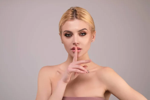 Young woman having secret while holding finger on lips and showing silence sign. Shh sign. Beautiful woman with silent sign. Studio shot, on studio background. Keep silence gesture