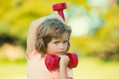 Güçlü pazı kasları olan sporcu çocuk. Spor yapan çocukların halterleri. Güçlü küçük çocuk parkta dambılla egzersiz yapıyor. Sağlıklı aktiviteler, çocuk yaşam tarzı