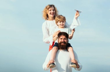 Baba anne ve oğlu dışarıda oynuyorlar. Yaz istihkakı. Sevimli küçük çocuk kağıt uçak tutuyor. Mutlu bir aile. Ebeveynler ve çocuk. Mutlu aile ve küçük oğlu mavi yaz gökyüzünde oynuyor