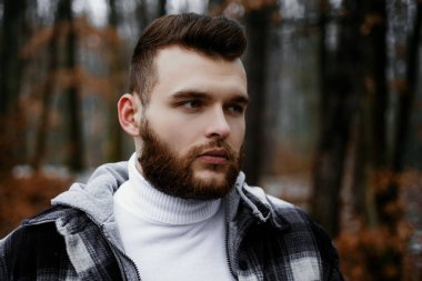 Lumbersexual kavramı. Sakallı oduncu damalı giysiler. Vahşi adam ormanda yürüyor. Hipster yaşam tarzı. Erkeklik ve vahşet. Oduncu tarzı. Şık adam oduncu. Bakımlı hipster.