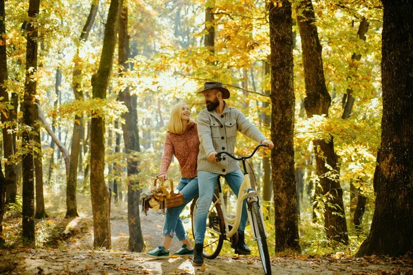 Couple in love ride bicycle together in forest park. Romantic date with bicycle. Bearded man and woman relaxing in autumn forest. Romantic couple on date. Date and love. Autumn date hike in forest.