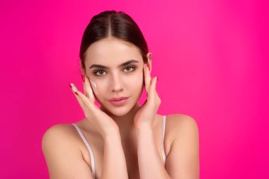 Young woman applying body cream against studio background. Beauty routine. Studio face of a beautiful woman with perfect skin. Wrinkle cream. Concept of beauty. Woman applying face cream