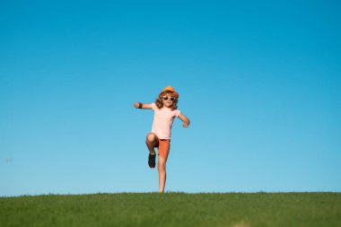 Çocuk bahar parkında mavi gökyüzü yakınlarında yeşil çimlerde koşuyor. Koşmak ve çocuklar için sağlıklı spor. Çocuk yaz parkında koşuyor. Açık havada antrenman yapıyorum. Çocuk sporcular