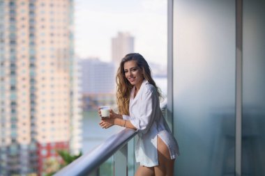 Young woman with glass of milk on balcony terrace. Girl drinking milk at home. Beautiful woman holding milk glass. Lactose free milk, concept. Morning beverage