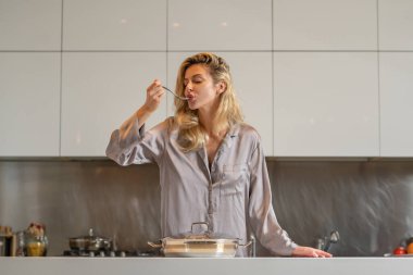 Çok fazla ev işi. Genç ev hanımı mutfakta yemek pişiriyor. Sabahları mutfakta tenceresi olan bir kadın.