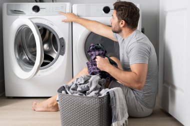 Çamaşır sepeti ve çamaşır makinesinin yanında kirli çamaşırları olan orta yaşlı bekar bir adam. Milenyum adamı çamaşır makinesine çamaşır koyuyor. Memnun olmayan İspanyol adam çamaşır makinesinde çamaşır yıkıyor.